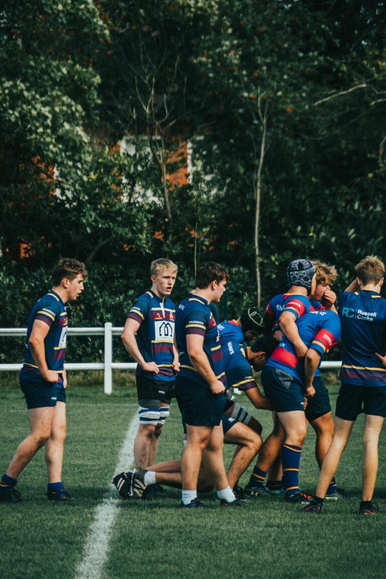 Team of young male athletes playing rugby outdoors, wearing blue uniforms.