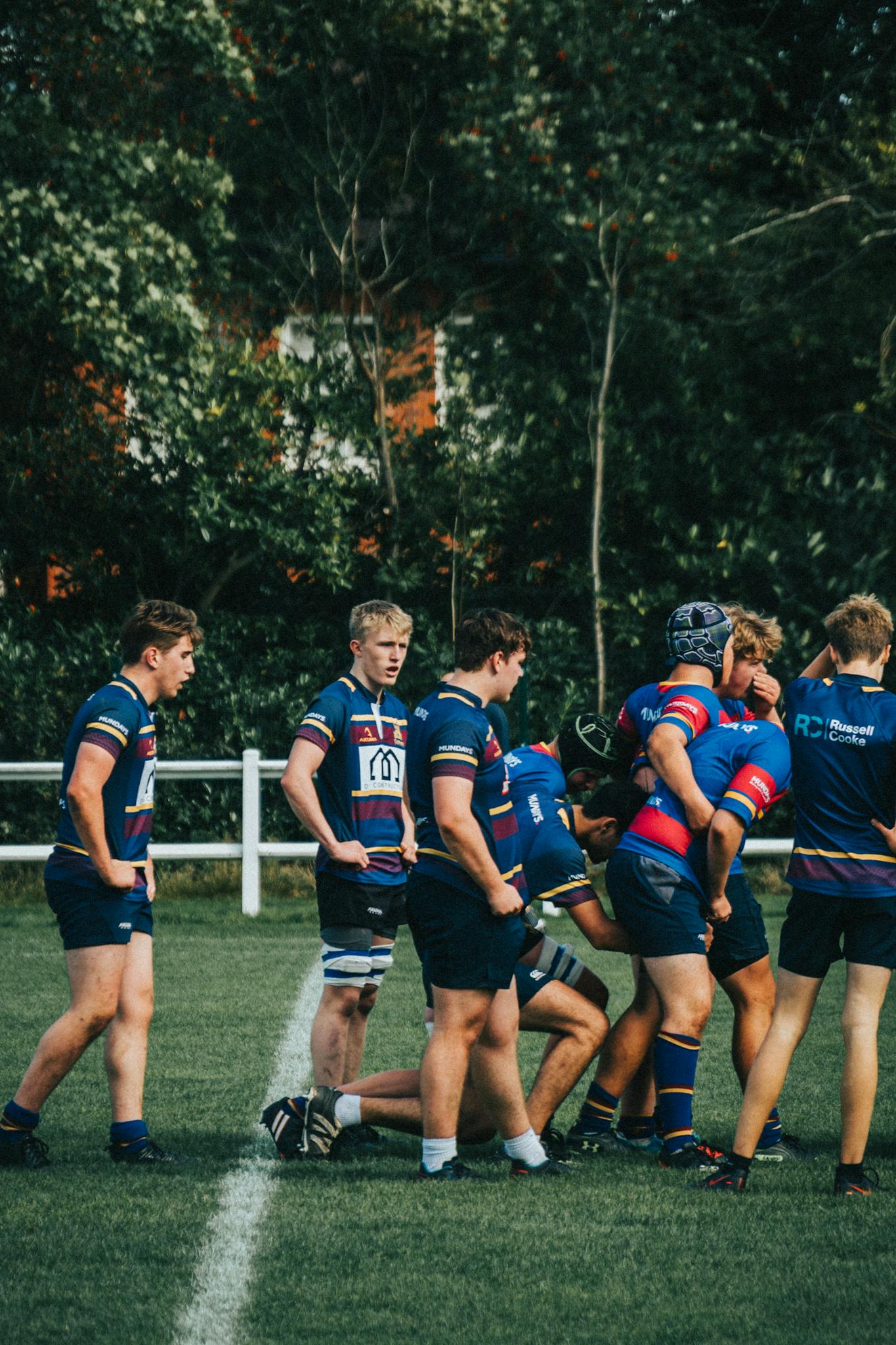 Team of young male athletes playing rugby outdoors, wearing blue uniforms.